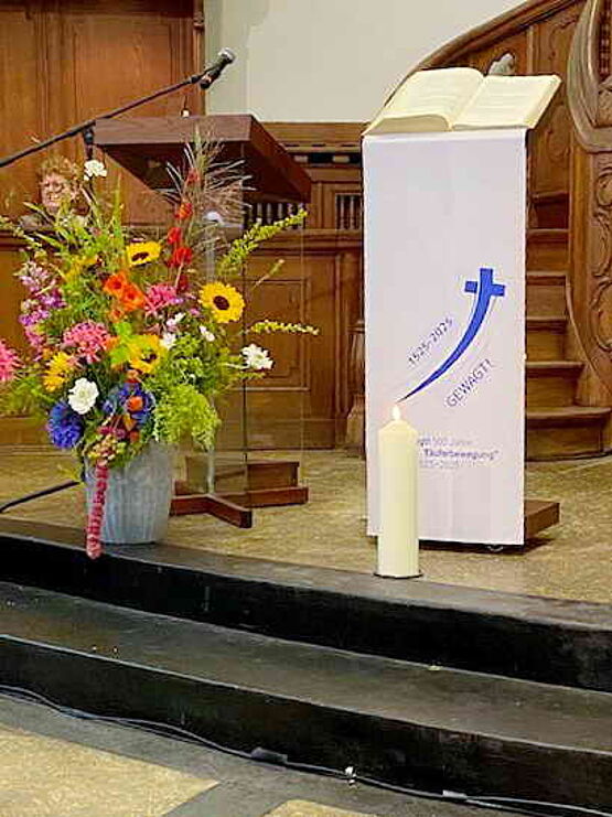 Blumenstrauß und Kerze vor dem Rednerpult in der Mennonitenkirche