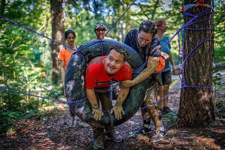 Junge Menschen, die einen jungen Mann durch einen hängenden Reifen hiefen