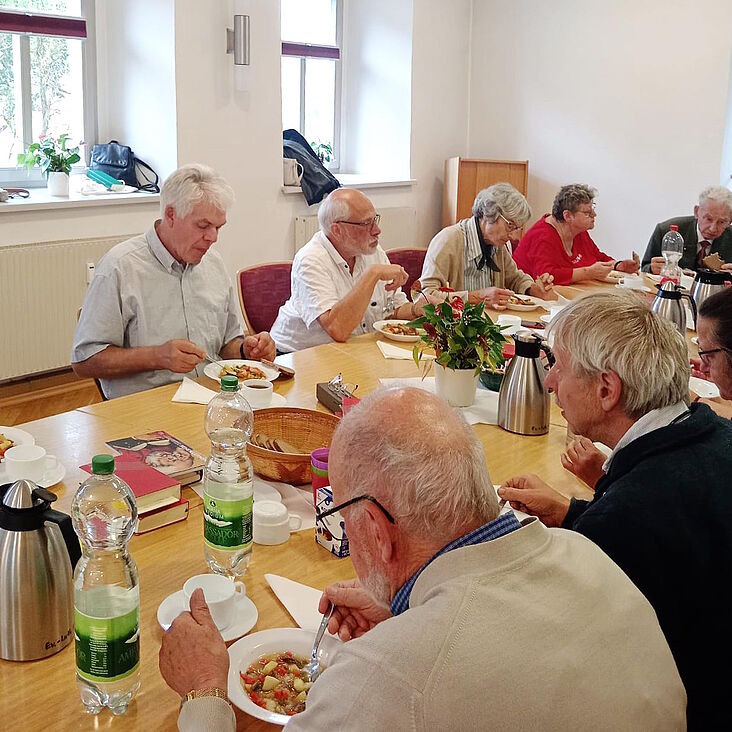 Menschen sitzen um einen Tisch und essen Suppe