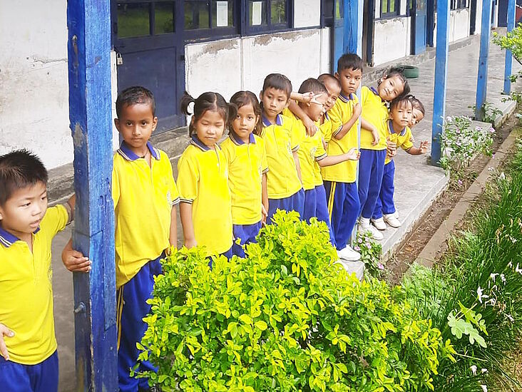 Schulkinder in Binnakandi nebeneinanderstehend, alle in gelben Shirts und blauen Hosen