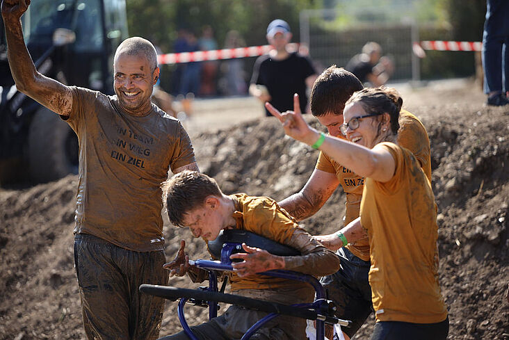 Drei jungeMenschen, die einen Jungen im Rollstuhl durch Schlamm schieben