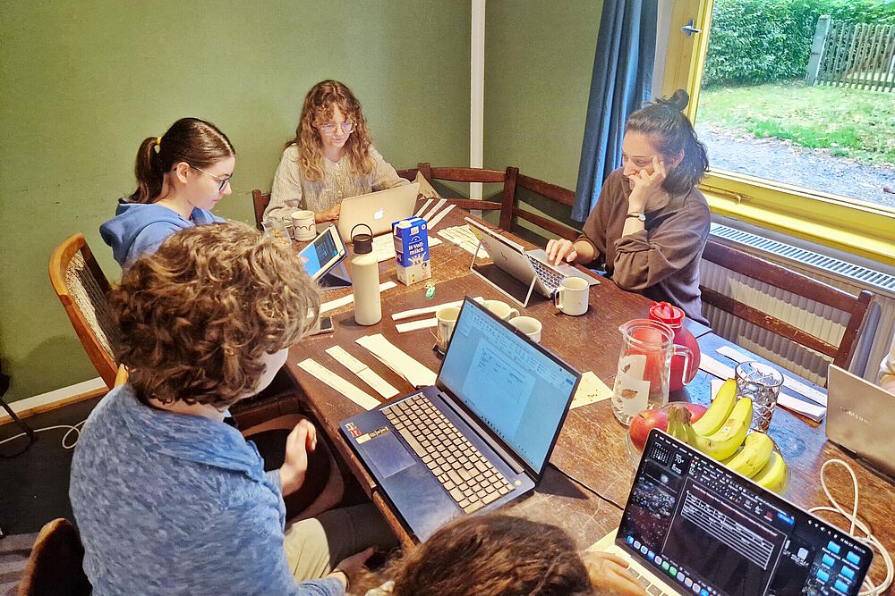 Teilnehmnede mit Laptops an einem Tisch sitzend