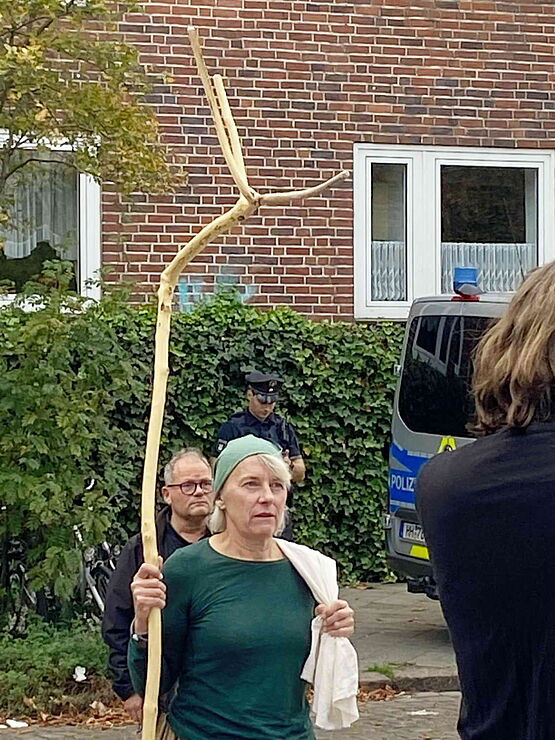 Frau mit langem und am oberen Ende dreifach gegabeltem Holzstab in der Hand