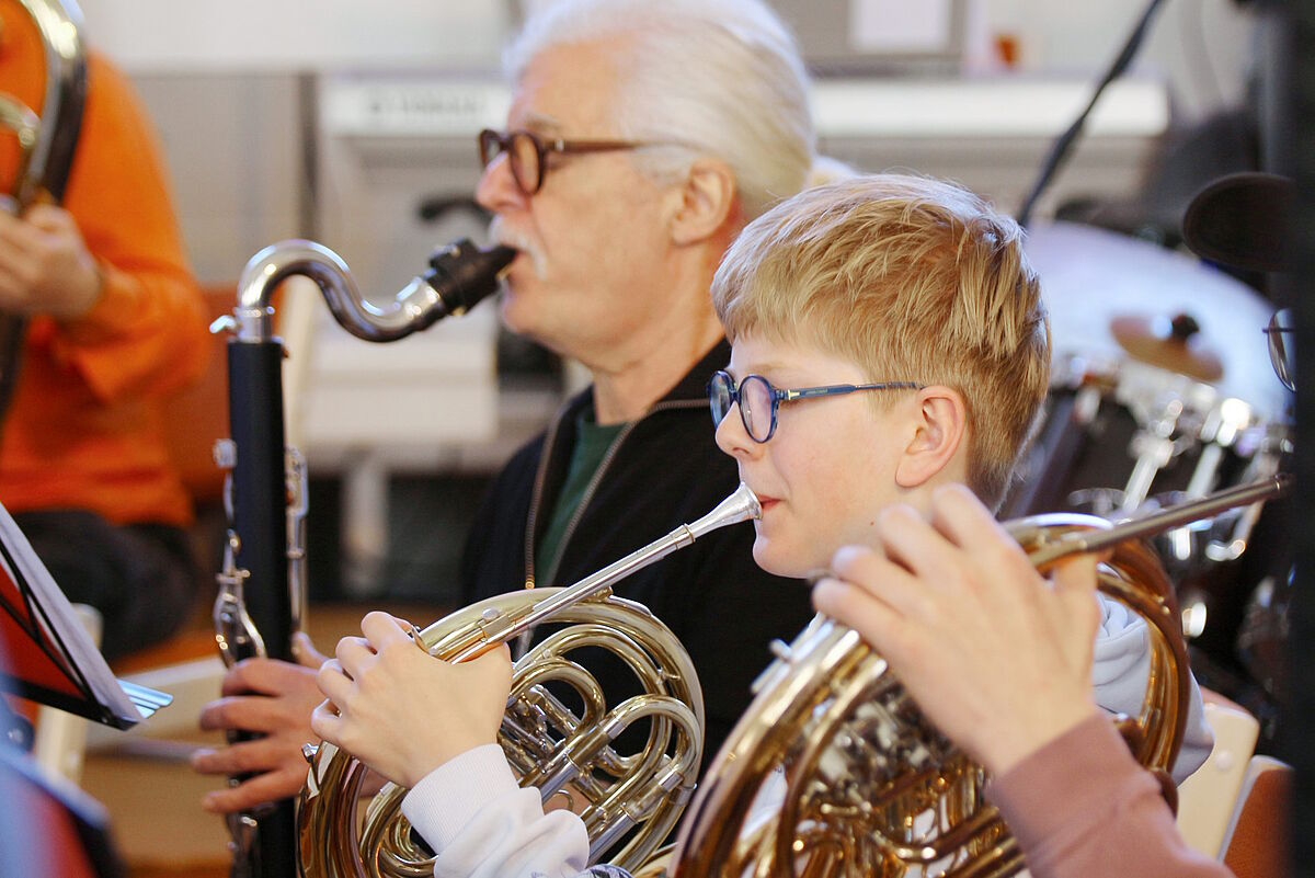  älterer Herr mit Saxophon, im Vordergrund Schüler mit Horn