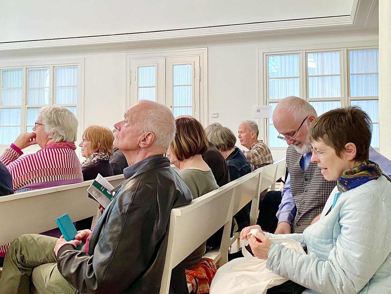 Besuch der Teilnehmer und Teilnehmerinnen auf weißen Bänken im Versammlungsraum der Sozietät Basel sitzend