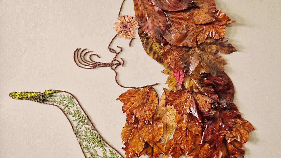 Ein Bild aus Laubblättern und anderen natürlichen Materialien, welche zusammen die Dartsellung einer Frau ergeben