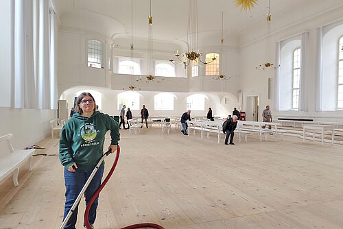 Frau mit Staubsauger im leergeräumten Kirchensaal