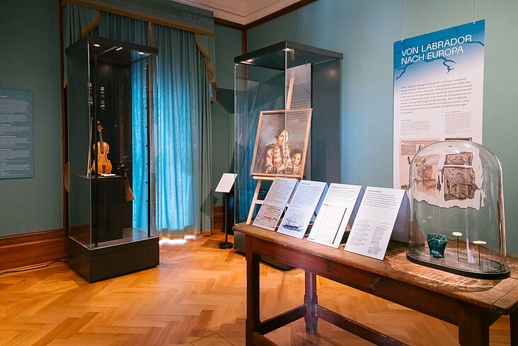 Im Ausstellungsraum  zu sehen sind u.a, eine Violine und ein Gemälde einer Inuit-Frau mit Kind
