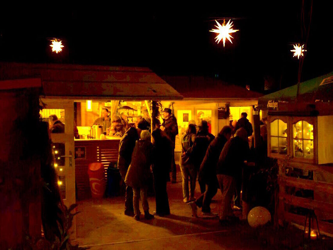 Besucher und Besucherinnen des Sternegartens bei Dunkelheit mit beleuchteten Hütten und Sternen