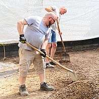 Orte für Begegnung schaffen Menschen im Kirchgarten, welche den Boden für den Bau eines Gartenhauses vorbereiten.