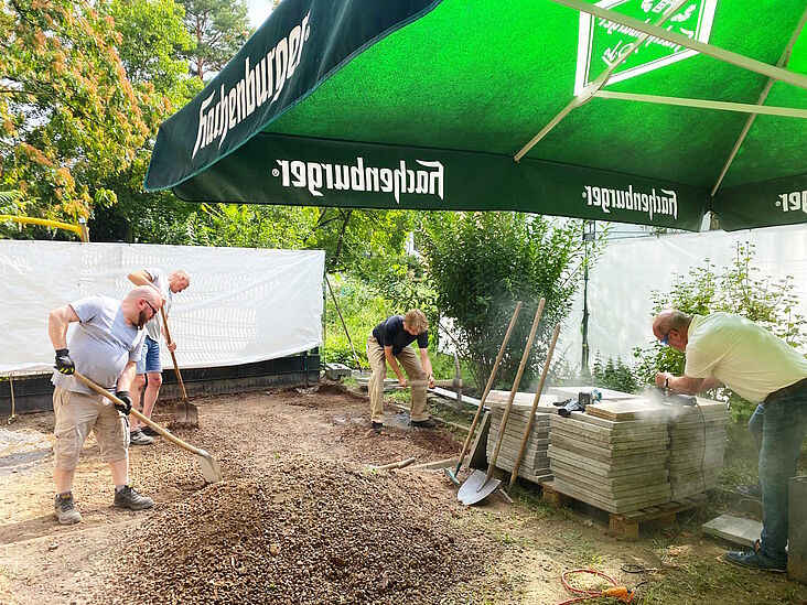 Menschen im Kirchgarten, welche den Boden für den Bau eines Gartenhauses vorbereiten.