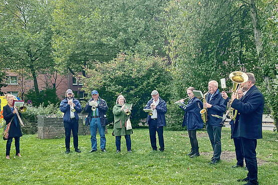 Spielender Bläserchor im Halbkreis auf einer Wiese stehend.