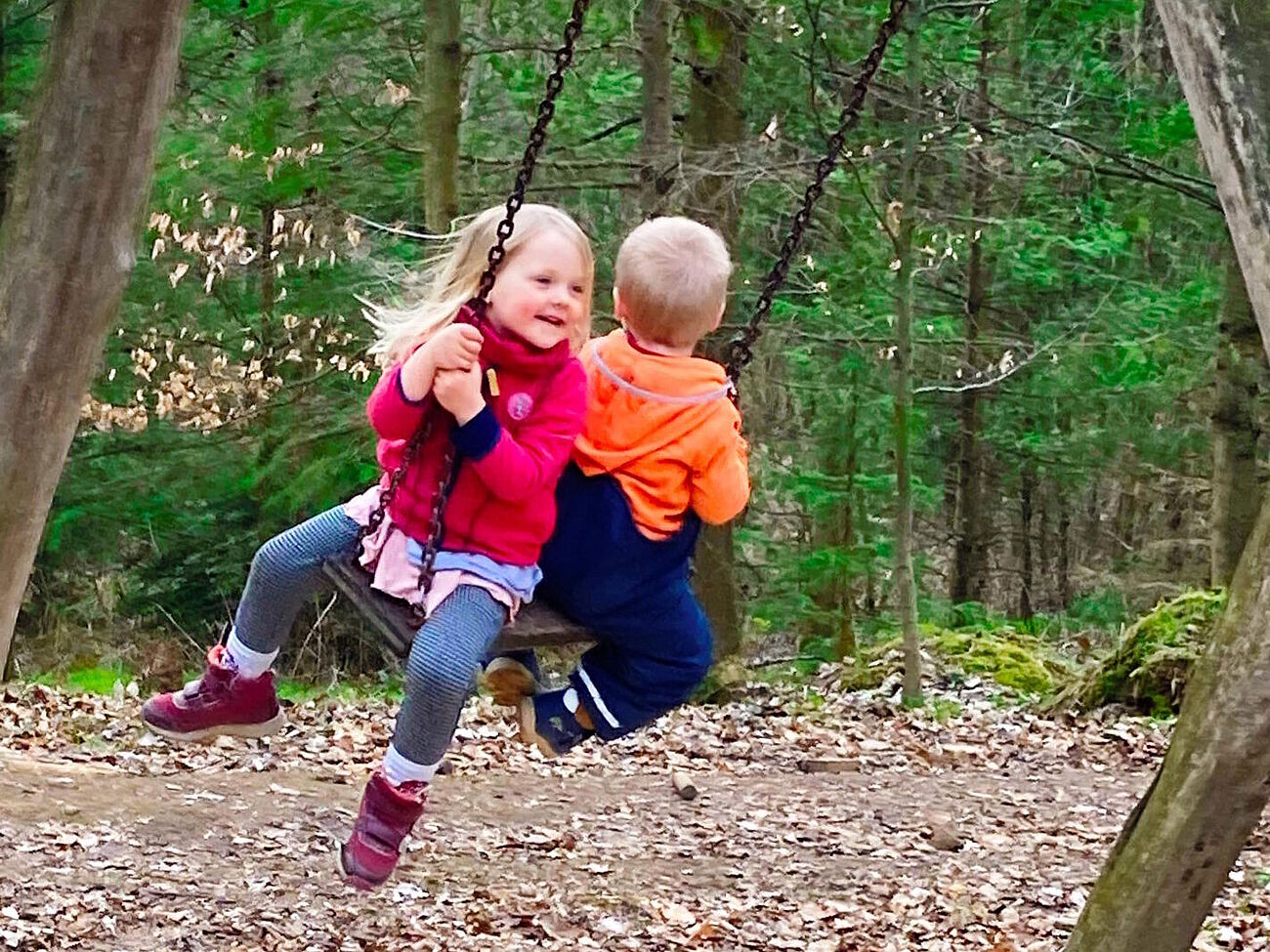 zwei Kinder Rücken an Rücken schaukeln sitzend auf einem Schaukelbrett