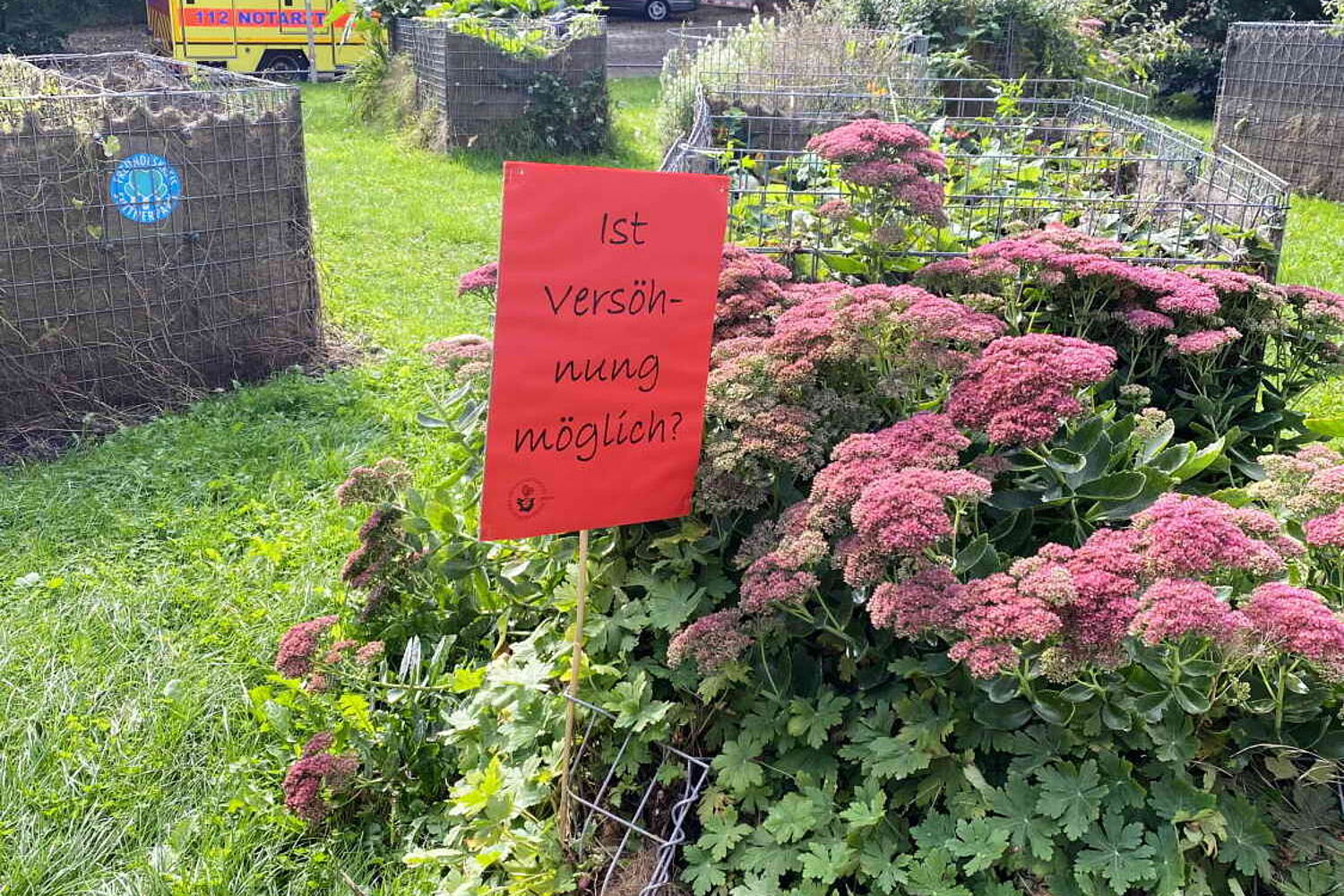 Die Frage "Ist Versöhnung möglich?" auf einem Schild im Blumenbeet.