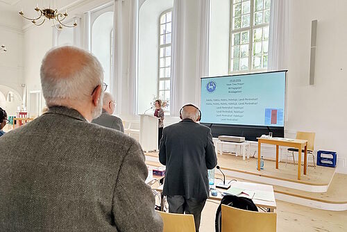 Von hinten sind zwei Männer zu sehen, die zum Mittagsgebet an ihren Plätzen stehen