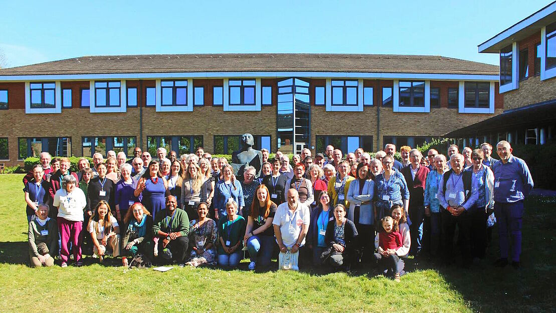 Gruppenbild aller Teilnehmenden auf einer Wiese, im Hintergrund das Konferenzhaus