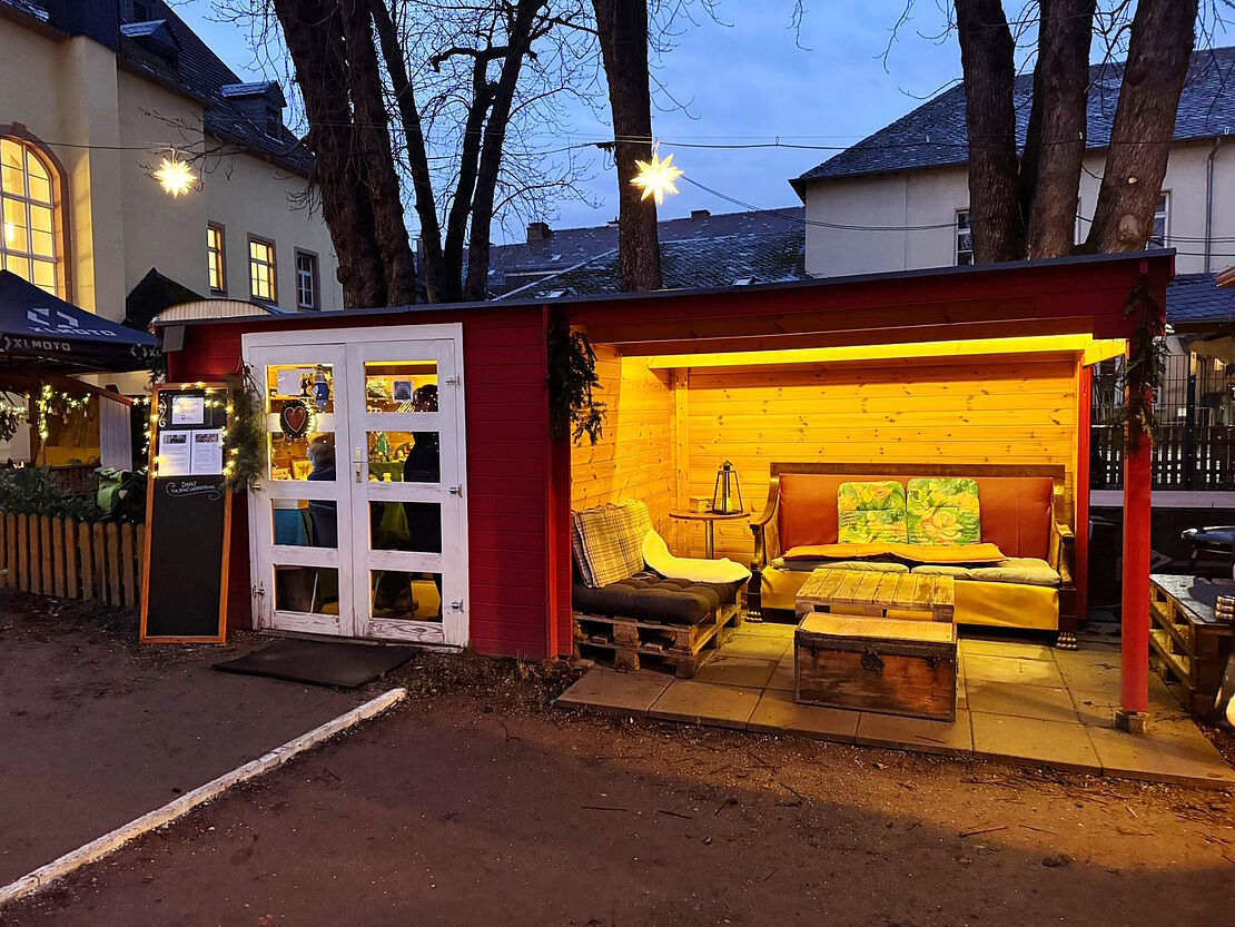 Eine beleuchtete Hütte am Abend mit überdachter Sitzecke.
