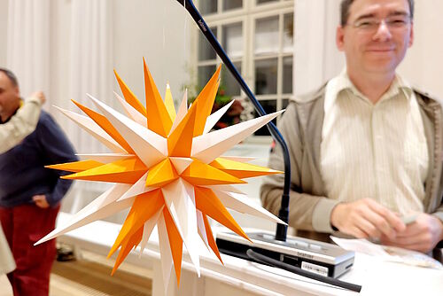 Papierstern mit gelben und orangen Zacken, im Hintergrund Jan König
