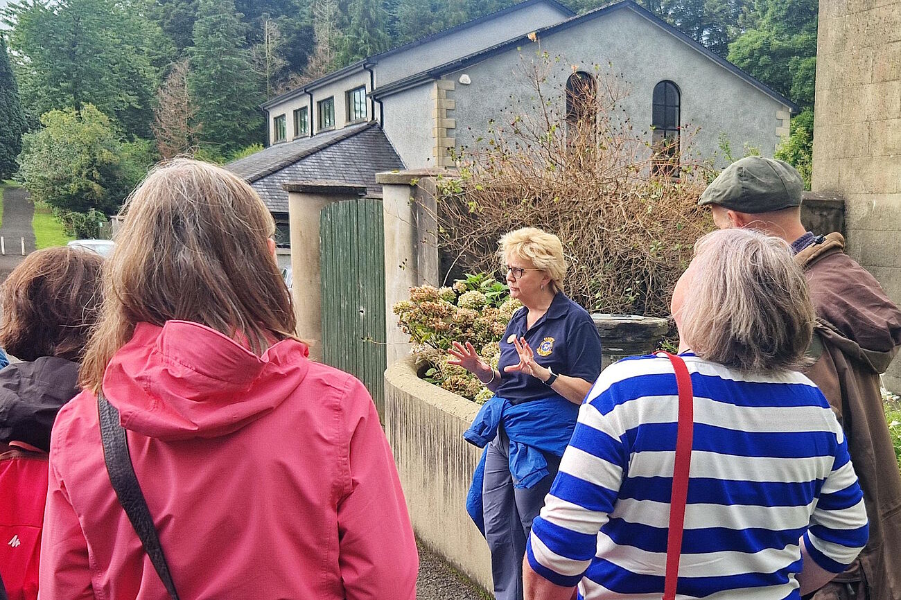 Rückenansicht einer Gruppe von Menschen, denen eine Touristenführerin etwas erzählt.