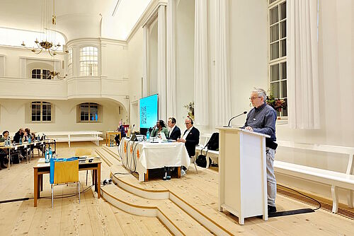 Mann an Rednerpult im Kirchensaal