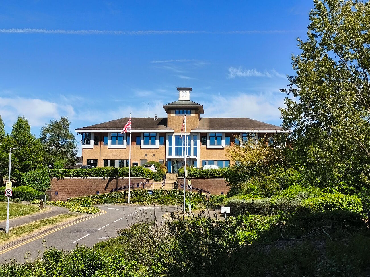 Blick auf das Training & Conference Centre in Milton Keynes mit dorthinführender Straße, im Vordergrund rechts Bäume und eine Wiese