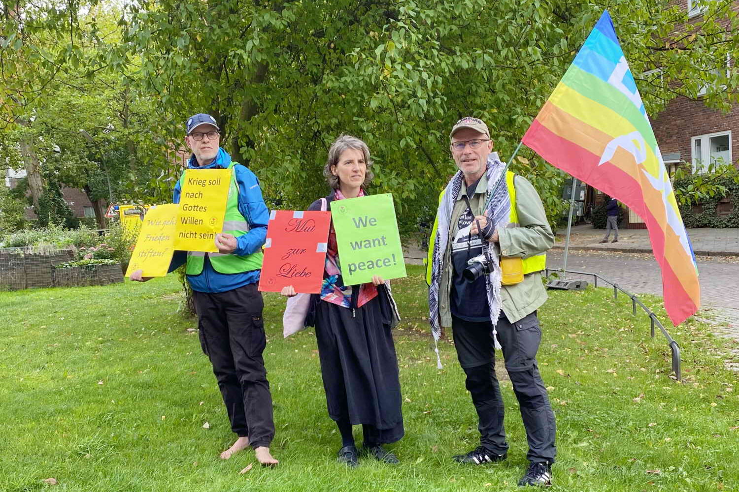 Eine kleine Gruppe Menschen mit einer Friedensfahen auf der Wiese stehend.