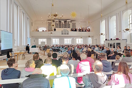 Blick in den gefüllten Kirchensaal Richtung Orgelempore, auf welcher der Kirchenchor zu sehen ist.