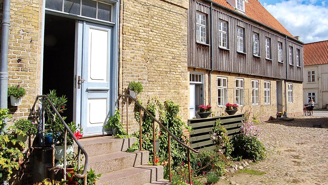 Blick auf das Brüderhaus, im Vordergrund ein historischer Hauseingang mit Treppe und Grünpflanzen