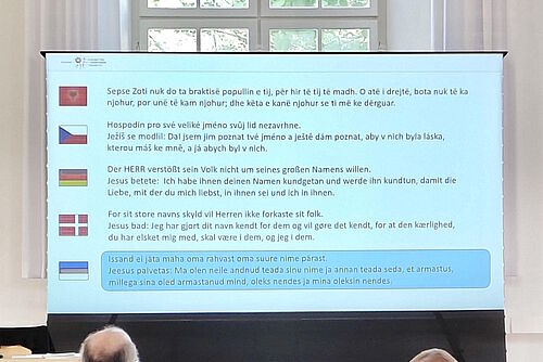 Großes Display im Kirchensaal, auf dem die Tageslosung in den Sprachen aller Teilnehmenden zu lesen ist