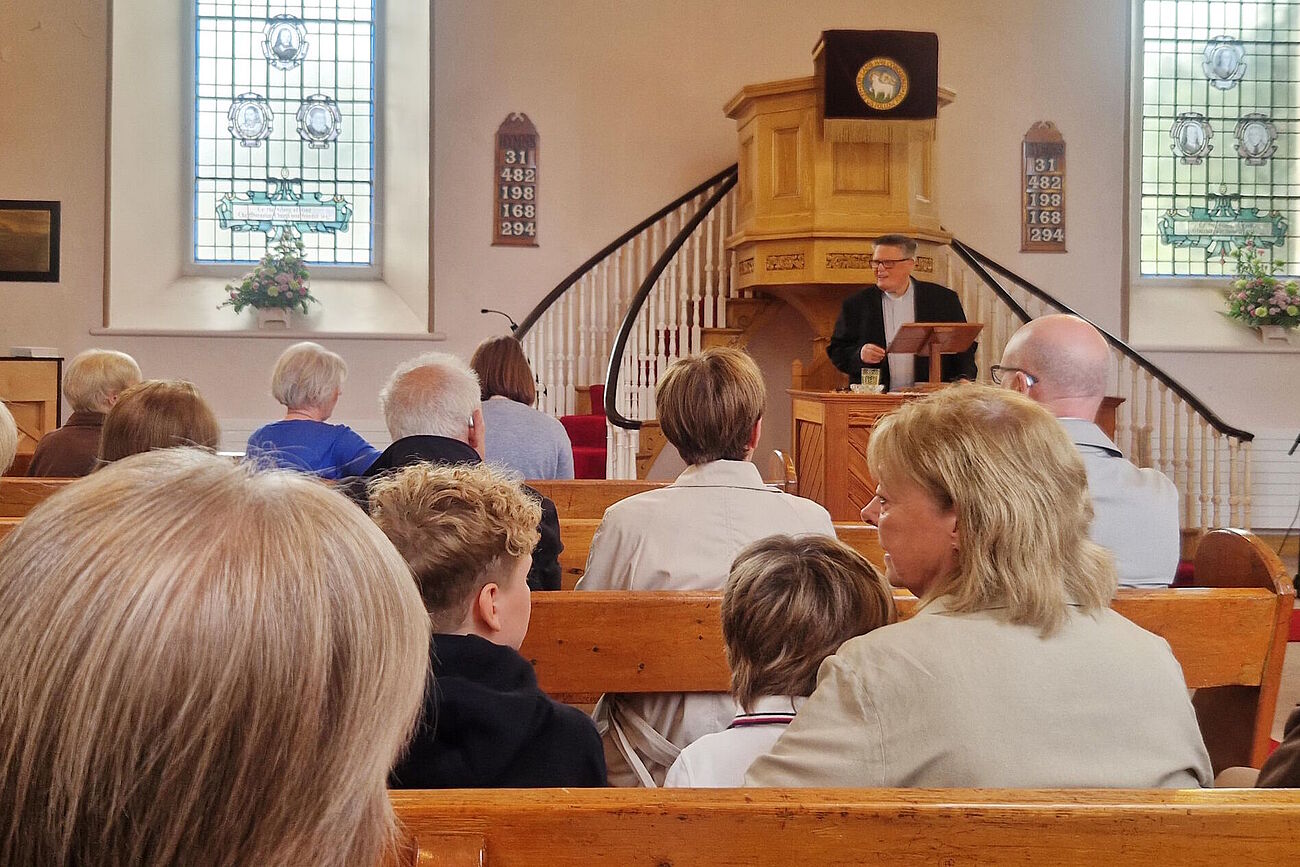 Menschen von hinten zu sehen sitzen auf den Kirchenbänken in der Kirche von Gracehill; vorne Predigt David Howrath