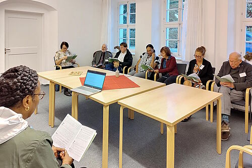 Acht Menschen sitzen mit Liedheften um einen Tisch