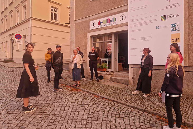 Teilnehmende und Gäste des Poetry Slams stehen in lockerer Runde vor den Schwesternhäusern in Kleinwelka