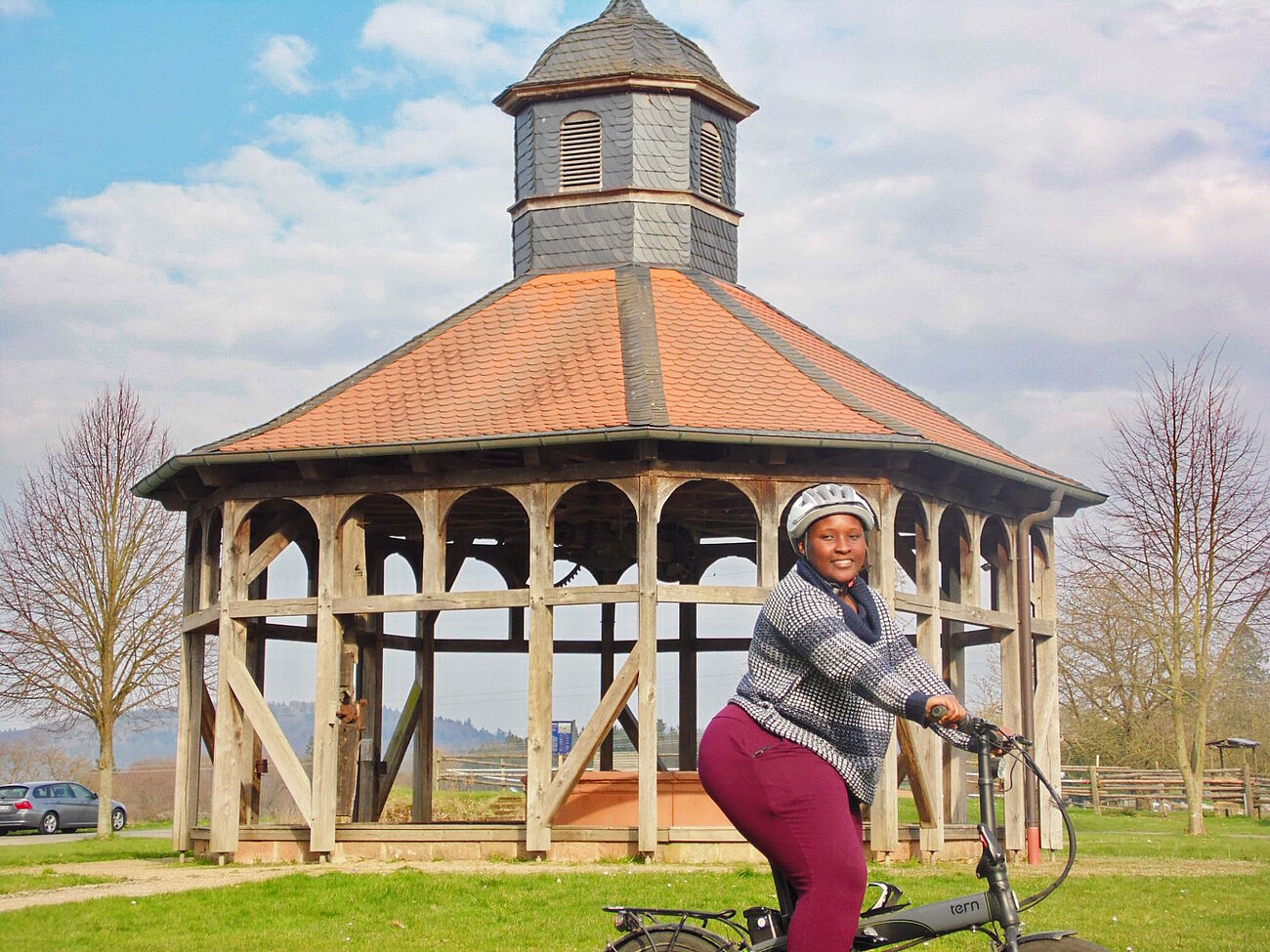 Odwa Sikisiki als freiwillige Mitarbeiterin auf dem Herrnhaag auf einem Fahrrad sitzend, im Hintergrund das Brunnenhäuschen.