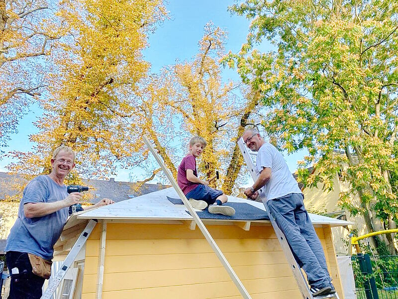 Zwei Männer und ein Junge beim befestigen der Dachkonstruktion.