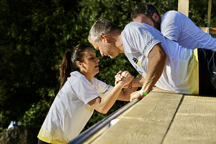 Ein Mann reicht einer Frau seine Hand, damit sie sich an ihr nach oben ziehen kann