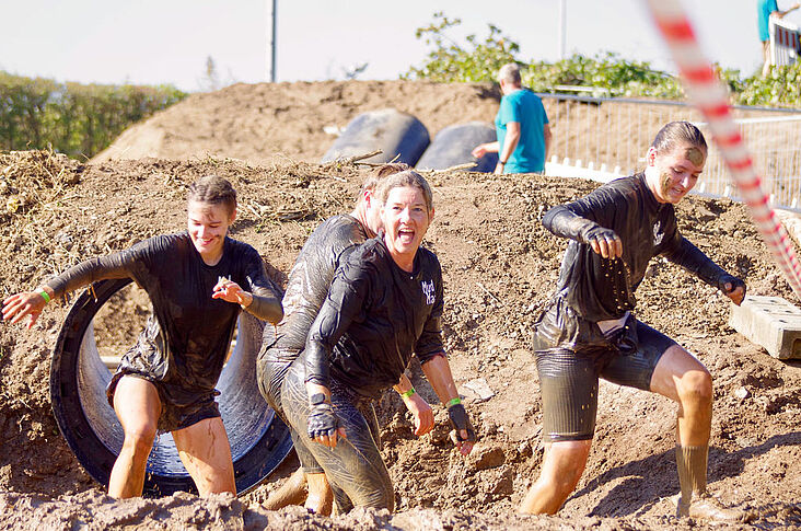 Drei junge Frauen die sich durch ein Schlammloch arbeiten