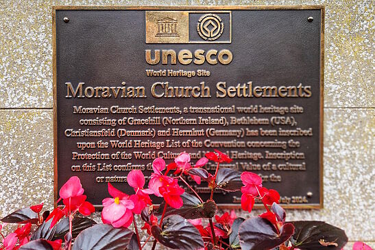 bronzene UNESCO-Plakette an der Wand, davor Blumen