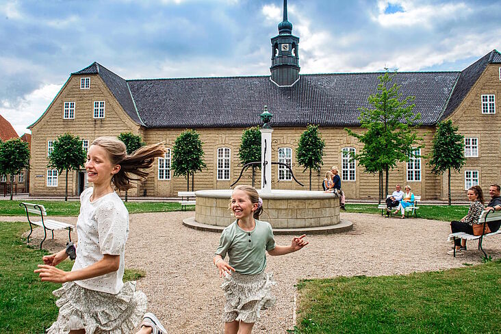Lachende Kinder laufen über den Zinzendorfplatz in Christiansfeld; im Hintergrund der Kirchensaal