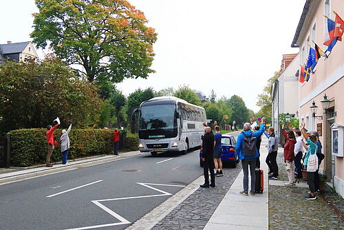 Winkende Menschen an beiden Straßenseiten, der fahrende Bus auf der Straße