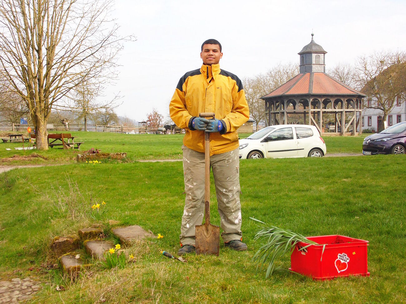 Eagan Marshand als freiwilliger Mitarbeiter auf dem Herrnhaag mit einem Spaten auf der Wiese stehend, im Hintergrund das Brunnenhäuschen.