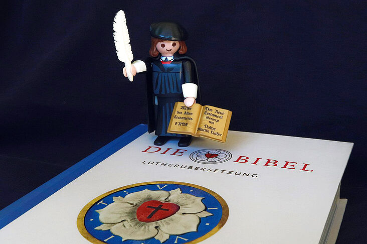 Martin Luther als Playmobil-Figur auf einer Luther-Bibel stehend