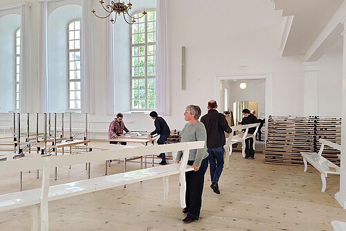 Freiwillige tragen Kirchenbänke aus dem Saal