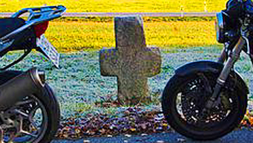 zwei Motorräder am Straßenrand stehend, dazwischen ein Steinkreuz am Wegesrand